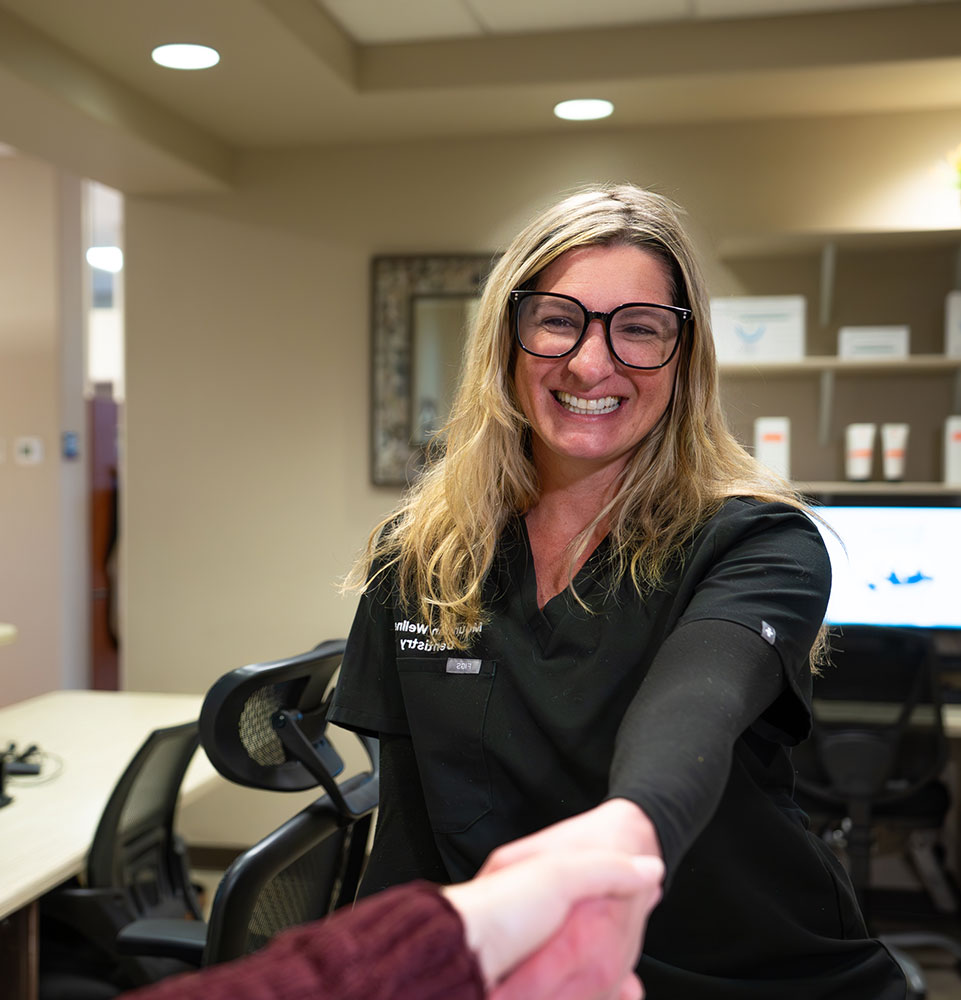 staff member smiling brightly while greeting dental patient at the front desk of the dental center