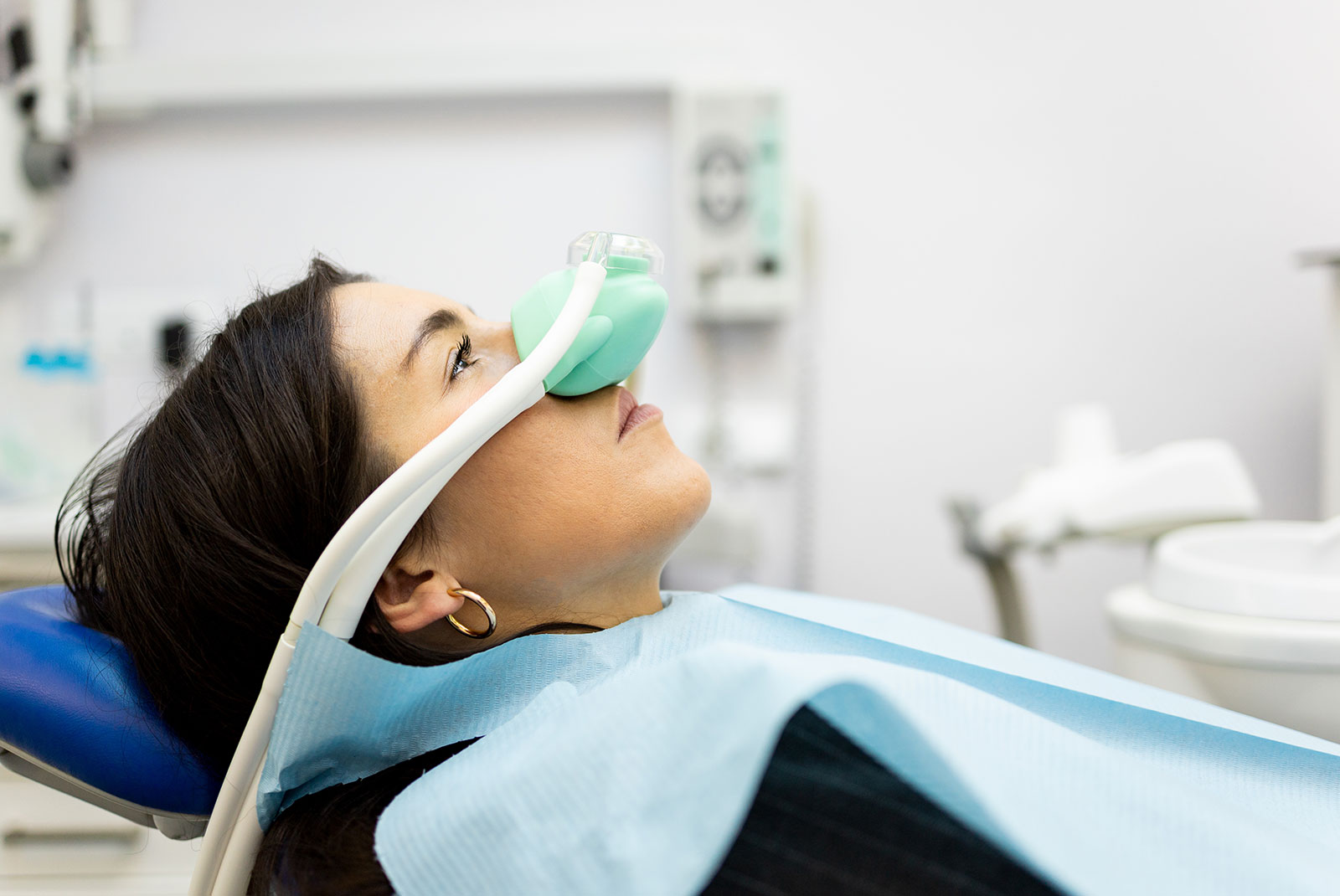 An adult woman sits in a dentist's office wearing a nasal mask to inhale nitrous oxide