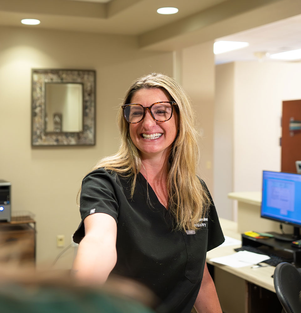 staff member smiling brightly while helping dental patient at the front desk of the dental center