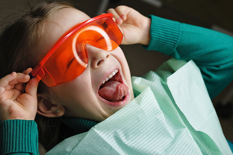Little girl sits in dental chair and wears protective glasses
